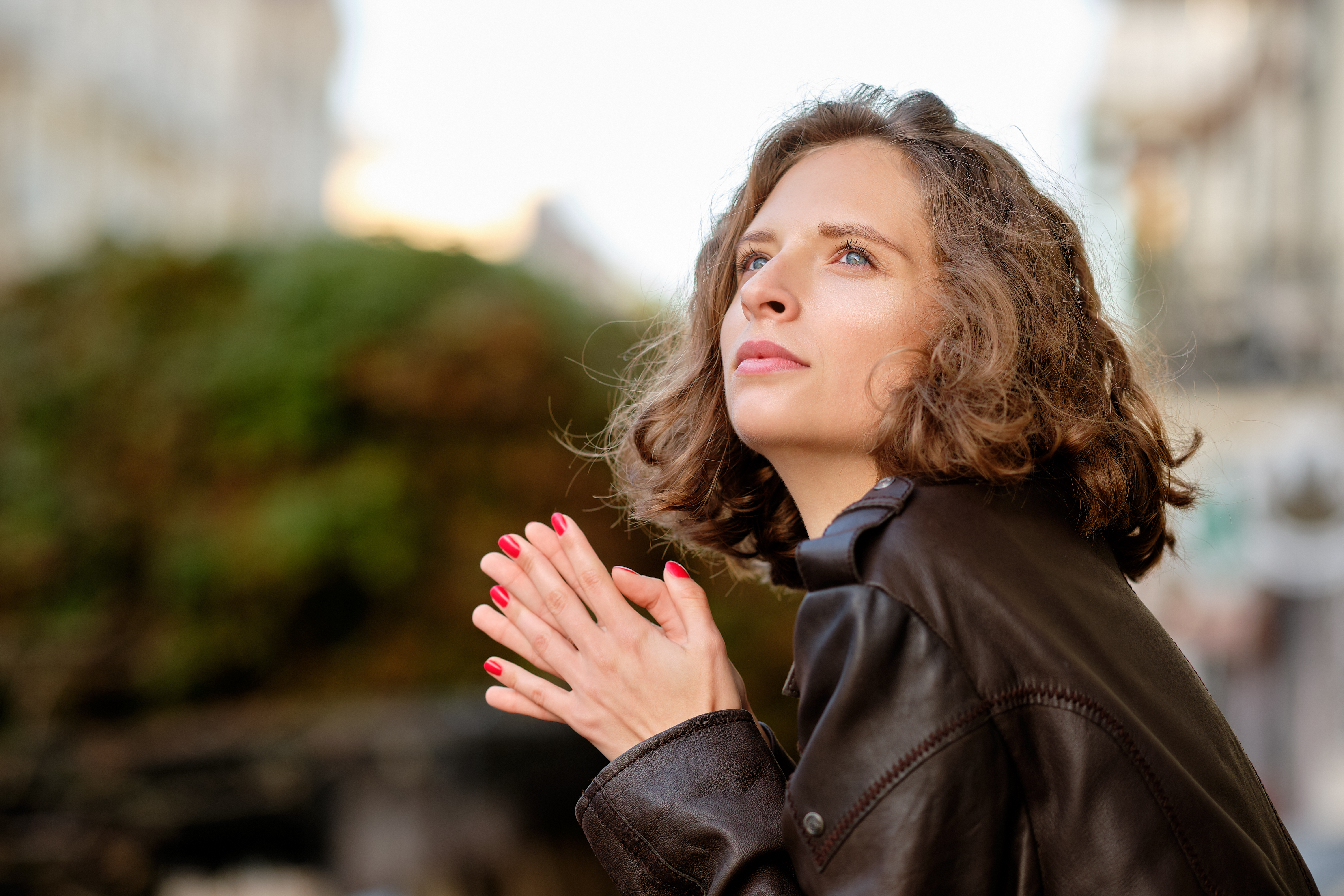 Femme en veste de cuir, mains jointes, regard tourné vers le haut